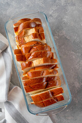 Sliced sweet bread in a baking dish on a gray concrete background. Recipe for bread pudding step by step.