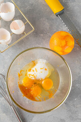 Mix of eggs, vanilla, sugar and orange peel in a bowl on a gray concrete background. Recipe for bread pudding step by step.