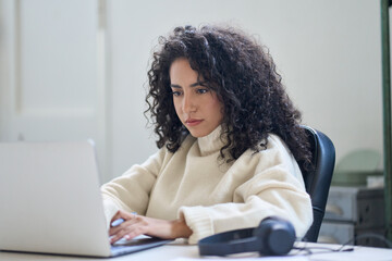 Focused young latin professional business woman office worker using laptop computer working online,...