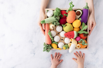 Mother giving baby wooden box with cute knitting vegetables and fruits for activity, motor and sensory development. Eco friendly toys concept.