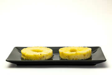 Two pineapple slices on a black plate.