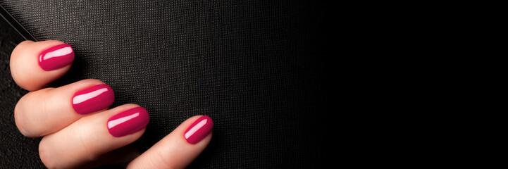 Female hand with beautiful manicure - viva magenta, pink nails on black leather surface background...