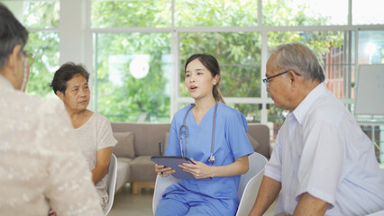 An Asian nurse talking to a group of old elderly patient or pensioner people smiling, relaxing,...