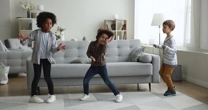 Three little multi ethnic boys dancing in living room, diverse cute children listen popular track, having fun together, moving to music enjoy carefree weekend at home. Pastime, hobby, active leisure