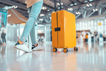Young female traveler passenger walking with a yellow suitcase at the modern Airport Terminal, Back...