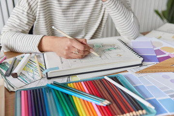 Cropped shot of unknown creative woman draws picture in album engaged in favorite activity develops her painting skills uses colorful crayons poses at table at home. Leisure pastime and hobby concept