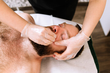 Obraz na płótnie Canvas Man receiving facial buccal massage in beauty salon.Beauty and skincare concept with a beautiful woman. Middle aged male relaxed with massage for facial lifting
