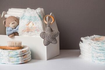 Wooden toys, a bear in a bow tie, a stack of diapers, a bottle and baby supplies on the changing table. Space for text.