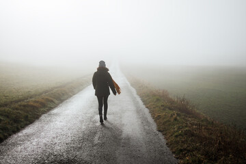 Lonely courageous woman walks on empty road in fog. Journey to unknown place and future