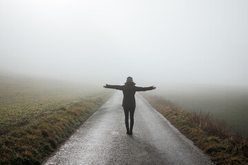 Woman with arms outstretched standing on empty road in fog