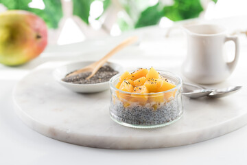 A light and airy view of a homemade mango chia pudding on a white marble board.