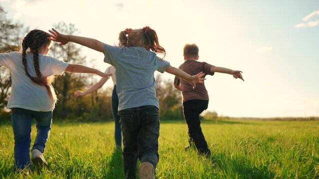 kids run in the park. a large group of a team of children running back view sunlight in the summer on lifestyle the grass in the park camera movement. people in the park happy family kid dream concept