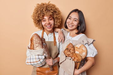 Horizontal shot of happy female bakers work together as team pose with loaves of freshly baked...