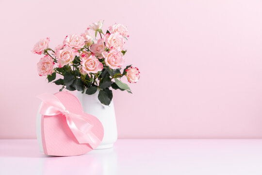 Beautiful bouquet flowers pink roses in vase and gift box with satin bow on pastel pink background table. Birthday, Wedding, Mother's Day, Valentine's day, Women's Day. Front view