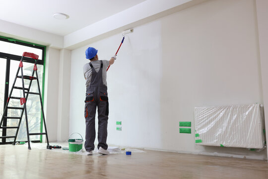 Professional painter paints office wall with roller brush.