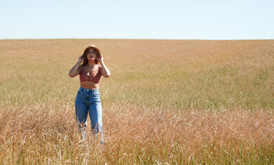 Hispanic woman wearing a hat posing on a wheat field on a sunny day