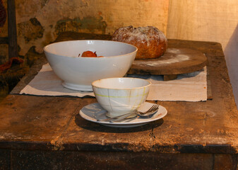 historical reconstruction of an ancient table set with bowl and bread in the old rural kitchen of the farm