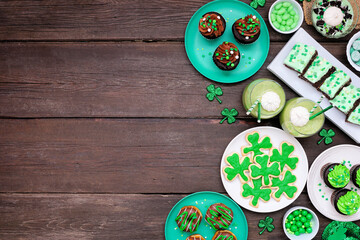 Fototapeta na wymiar St Patricks Day theme desserts. Side border against a dark wood background. Shamrock cookies, green cupcakes, brownies, donuts and sweets. Above view. Copy space.