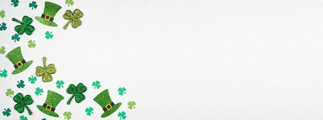 St Patricks Day shamrock and green leprechaun hat corner border. Overhead view over a white banner background with copy space.