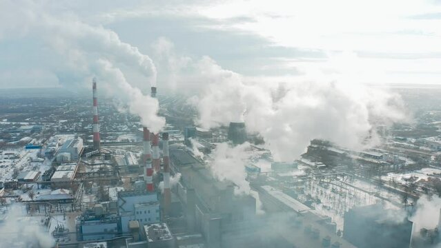 Drone flying to the left with a view of a thermal power plant with smoking chimneys against the backdrop of a city in smog and snow in a frosty winter