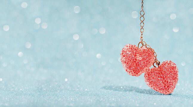 Two Red sparkling crystals heart pendants, valentine day greeting card. Bokeh blue abstract background. Valentines Day card or winter wedding