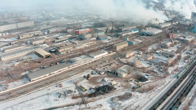 An industrial zone with factories, warehouses, a railroad with wagons and smoking chimneys of heavy industry. Cold winter and snow on the industrial zone.
