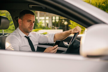 Businessman in a car. Work on the road. Using smartphone and laptop computer.