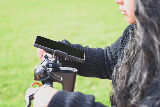 young latina woman, riding an electric scooter and using smartphone