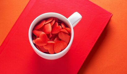 white cup full of hearts on red book and orange background