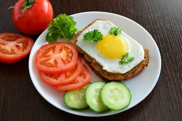 healthy sandwich with fried egg with yellow yolk on white plate with sliced vegetables