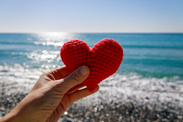 Red crochet heart in hand in front of blue sunny sea