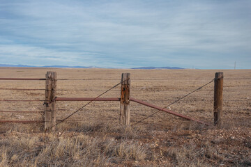 Fototapeta na wymiar Vintage wooden cattle fencing in front of large pasture with cloudy sky in rural New Mexico