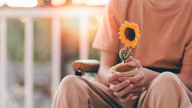 Crochet pot of sunflower in hands of young man with disability on wheelchair, sharing, caring Understanding and accepting equality respect for differences, love and valentine concept.	