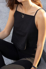 Young stylish happy brunette woman sitting on a busy business urban street in black sleeveless top and pants. Street style photoshoot.