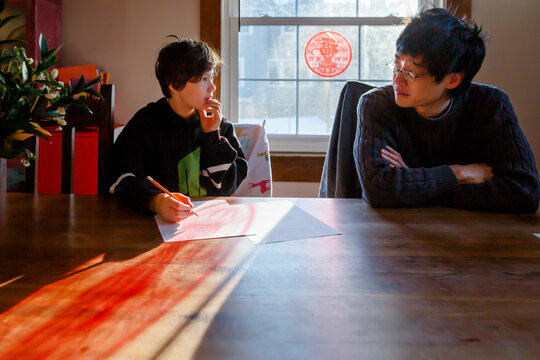 A father sits at table with son working on homework