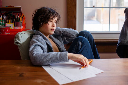 A boy in Cardigan sits at table by window working on homework