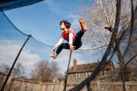 A happy boy does split jump on trampoline outside