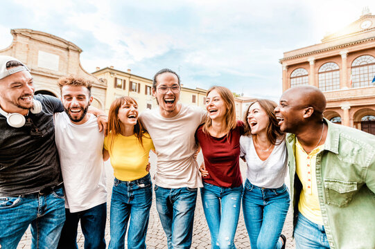 Group of lively young people laughing happily while walking together in the city - Smiling multiracial friends hugging each other while touring the city on vacation - Fun, holiday lifestyle concept.