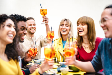 Young millenial people toasting spritz at cocktail bar garden patio - Trendy beverage life style concept with friends having fun together toasting fancy drinks on happy hour time - Bright warm filter