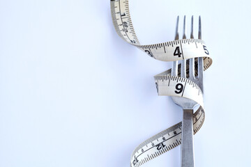 Measuring tape around fork on white background. Overweight problem. Diet and fasting. Weight loss. Copy space for text.