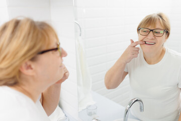 Caucasian woman in a white t-shirt in the morning looks in the mirror and smiles examining her teeth