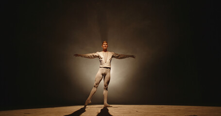 Handsome caucasian male ballet dancer performing pirouette and spinning on stage, wearing white tights, spotted by searchlight and isolated on black background 