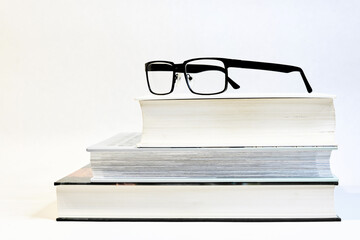 drei dicke Bücher auf einem Tisch mit einer Brille als Sehhilfe und einem weißen Hintergrund 