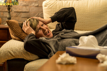 mujer mediana edad enferma con dolores  en el sofa de casa tapada con una manta, tomando medicina mirando el movil y el ordenador