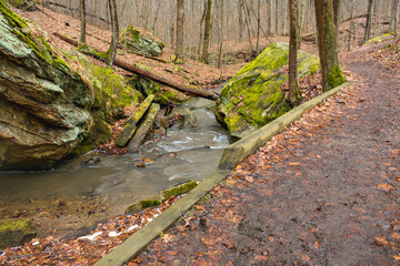 Path and stream in winter forest with large stones.