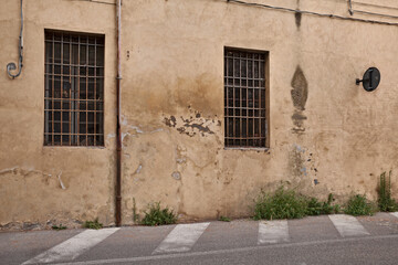 old wall with peeling paint, scratched stained plaster and closed windows - grunge background, urban decay