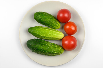Ripe tomatoes and cucumbers on a plate, on a white background. The concept of cooking, organic vegetables.