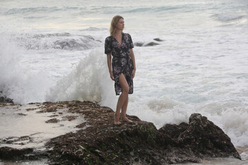 Fototapeta premium Portrait of beautiful young woman in dark floral wrap dress on wild rocky beach 
