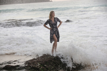 Fototapeta premium Portrait of beautiful young woman in dark floral wrap dress on wild rocky beach 
