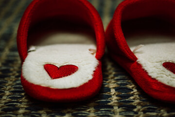 Red housewares slippers with heart symbols on a green blue carpet. A pair of home fluffy fuzzy...